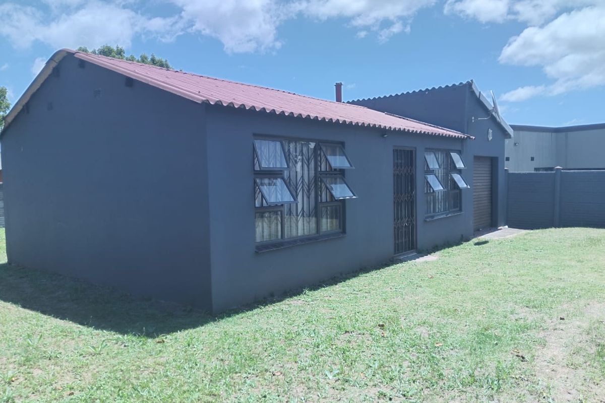 Rear view of a detached house featuring a tiled roof, security gates, burglar bars, and an attached garage, set within a private garden area.