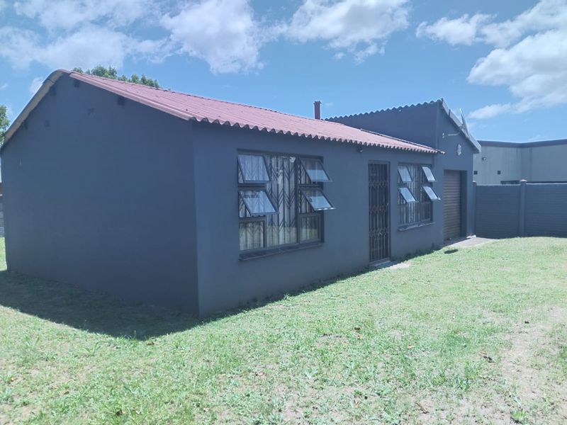 Rear view of a detached house featuring a tiled roof, security gates, burglar bars, and an attached garage, set within a private garden area.