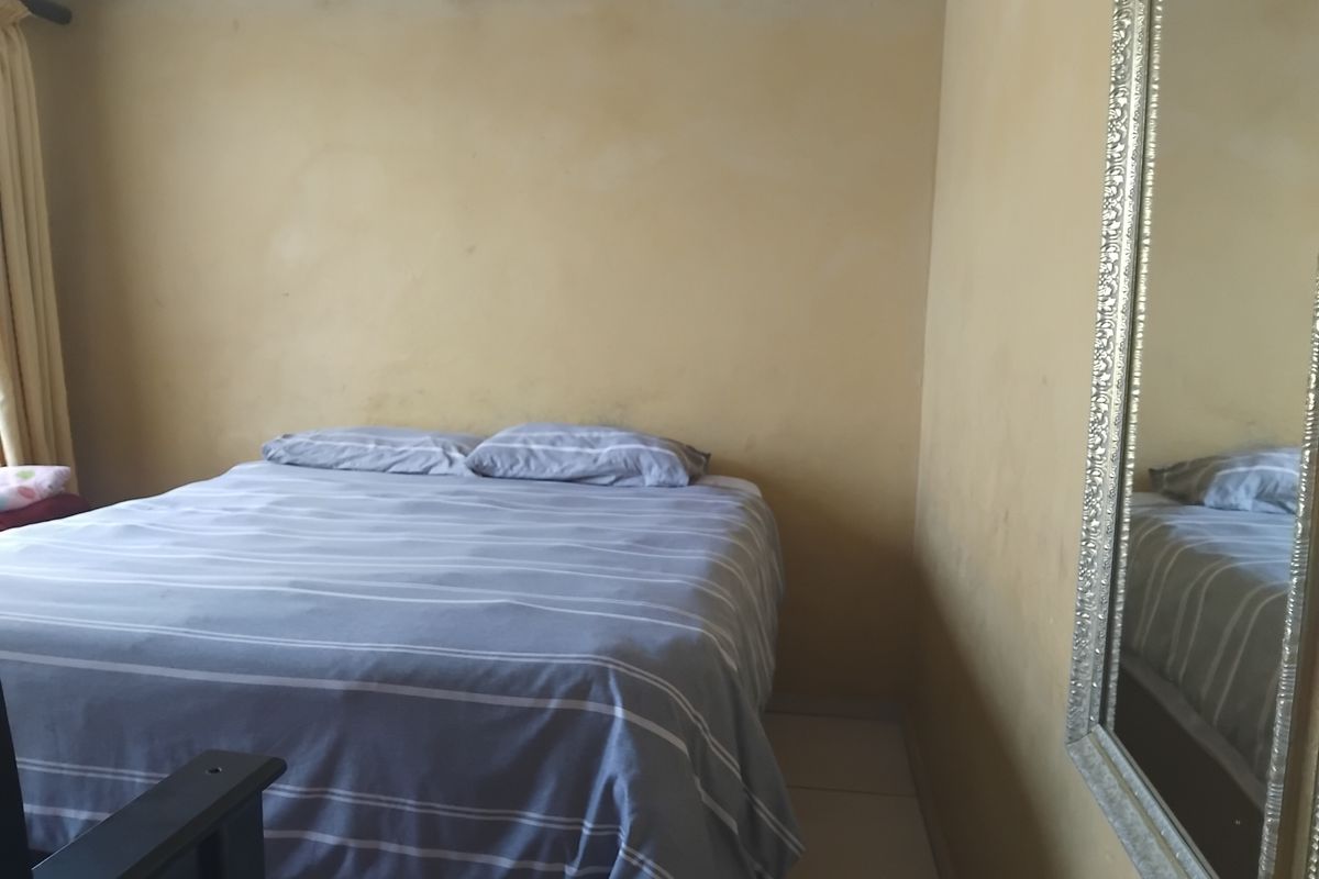 A bedroom featuring tiled flooring and coving, with walls showing signs of uneven paint application and wear.