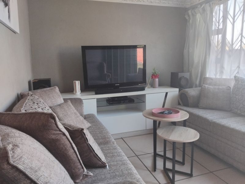 A comfortable living room featuring tiled flooring, decorative ceiling cornices, and a window fitted with a security gate.