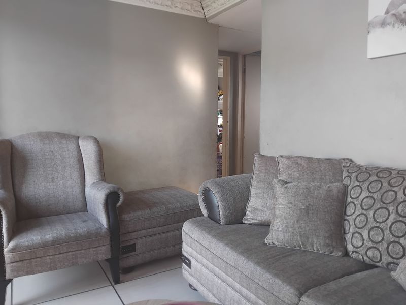 A living room area featuring tiled flooring and decorative ceiling cornicing, with neutral wall tones and a view into an adjacent hallway.