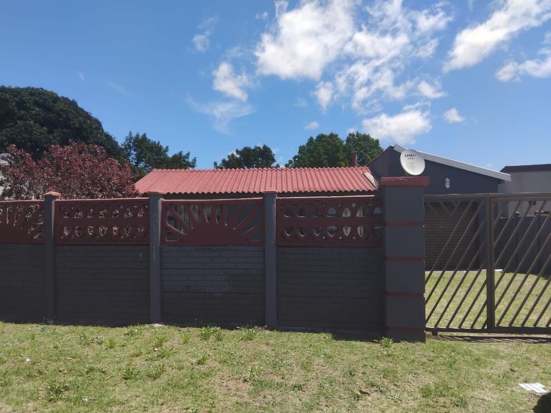 Front view of the property featuring a brick boundary wall, metal driveway gate, and a corrugated metal roof.
