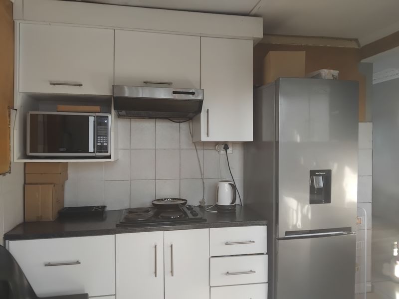 A compact kitchen featuring white cabinetry, a tiled backsplash, and built-in appliances, requiring minor cosmetic repairs to finishes and trim.