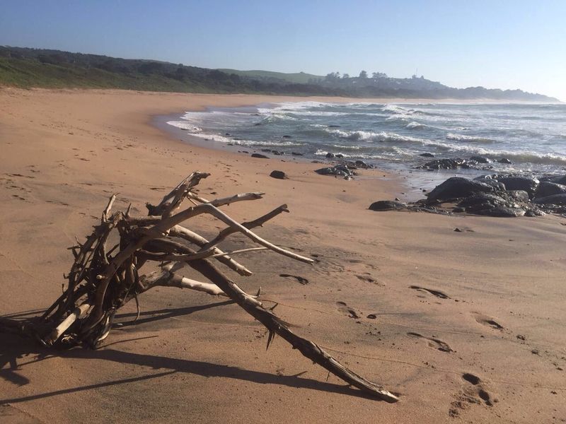 A scenic view of the coastline featuring sandy beach, rocky outcrops, and ocean waves.