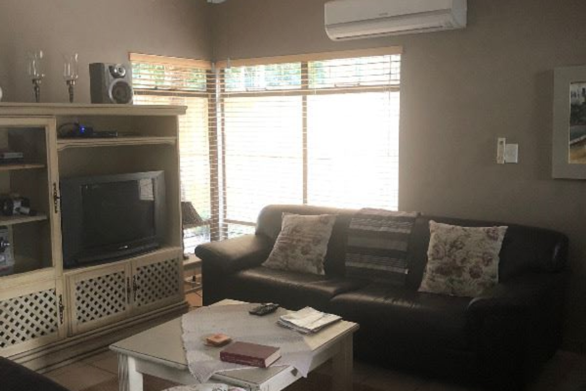 A comfortable living room featuring tiled flooring, a ceiling fan, and a wall-mounted split-system air conditioner for climate control.