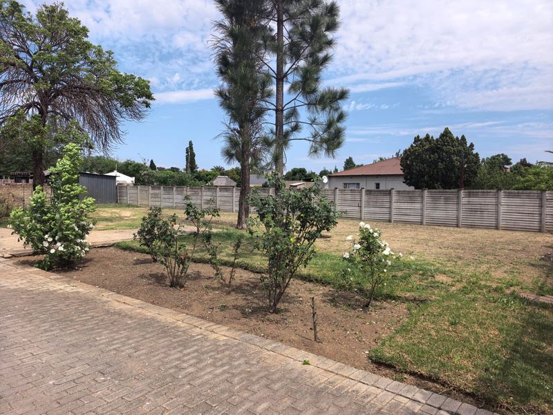 A spacious backyard featuring a paved walkway, established trees, and a secure precast concrete boundary wall.