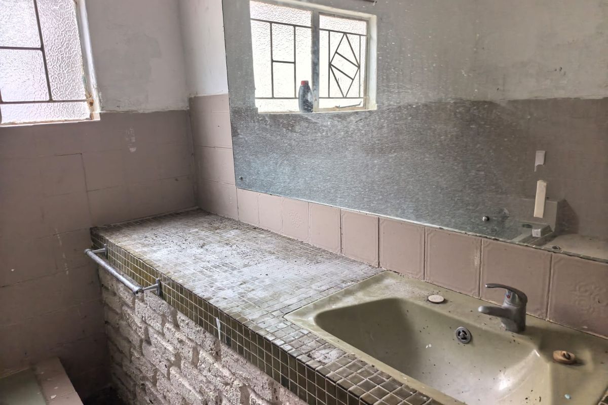 A dated bathroom vanity area featuring a tiled countertop, built-in basin, and wall-mounted mirror, requiring significant renovation and cosmetic updates.