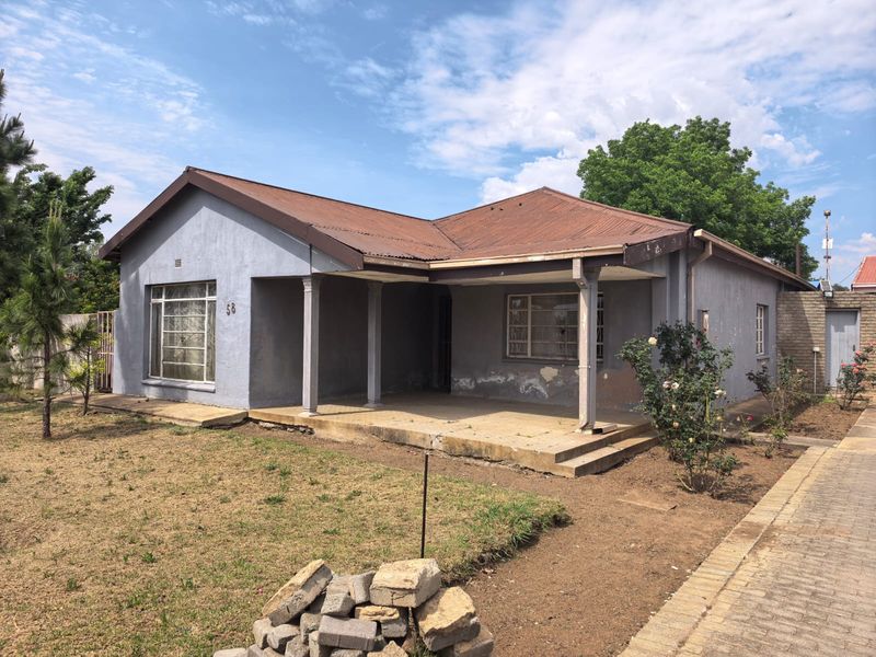 Front elevation of a single-story house featuring a covered porch, metal roofing, and steel-framed windows, set on a property with a paved driveway.