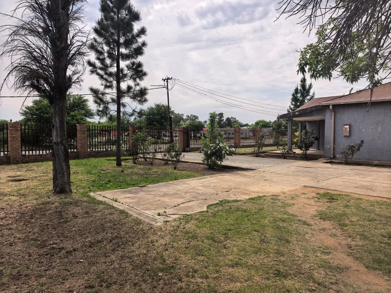 Front exterior view of the property featuring a concrete driveway, brick boundary wall with security fencing, and a covered entrance porch.