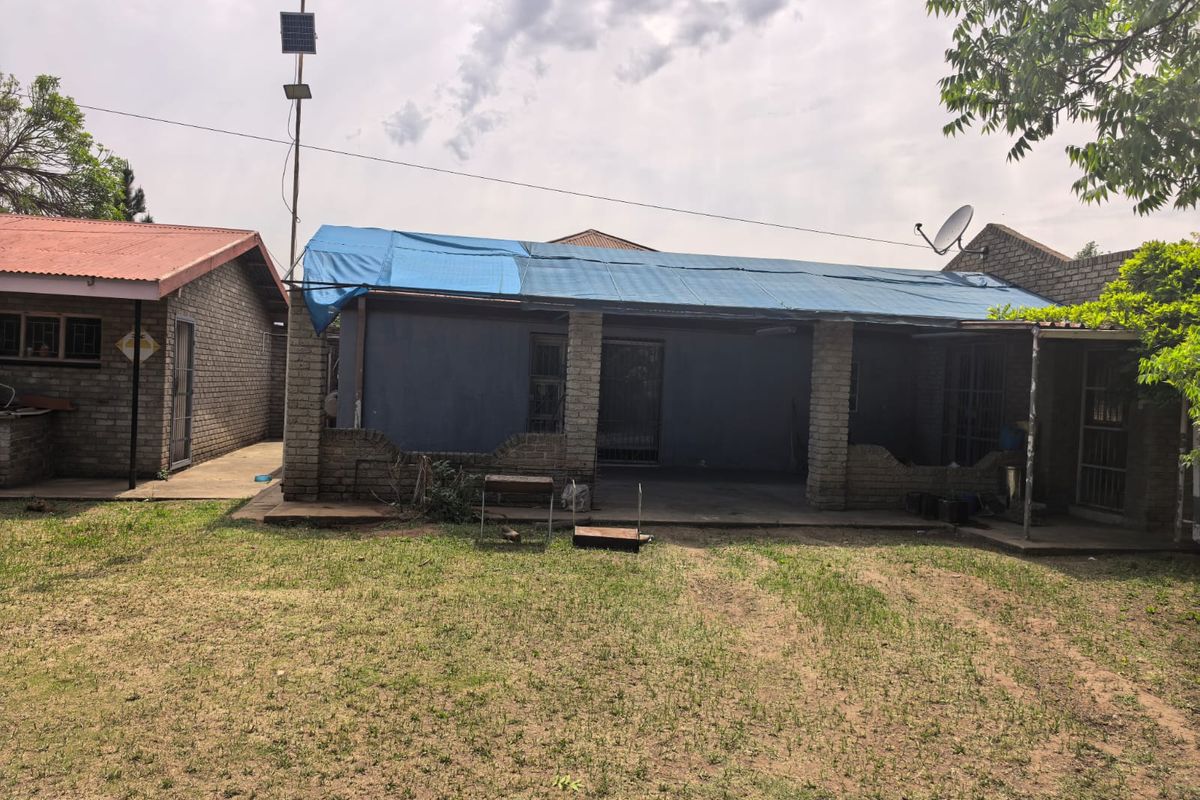 Rear view of the property featuring a covered patio area with brick pillars and a damaged roof section covered by a blue tarp.