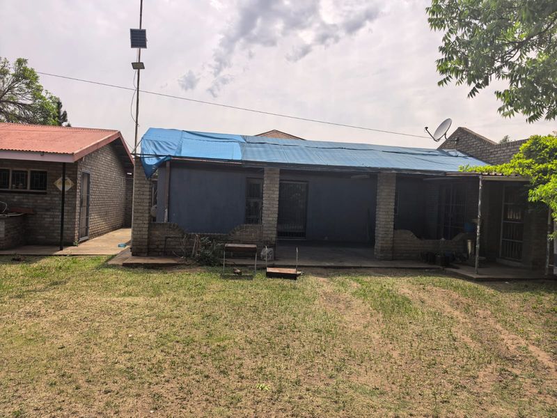 Rear view of the property featuring a covered patio area with brick pillars and a damaged roof section covered by a blue tarp.
