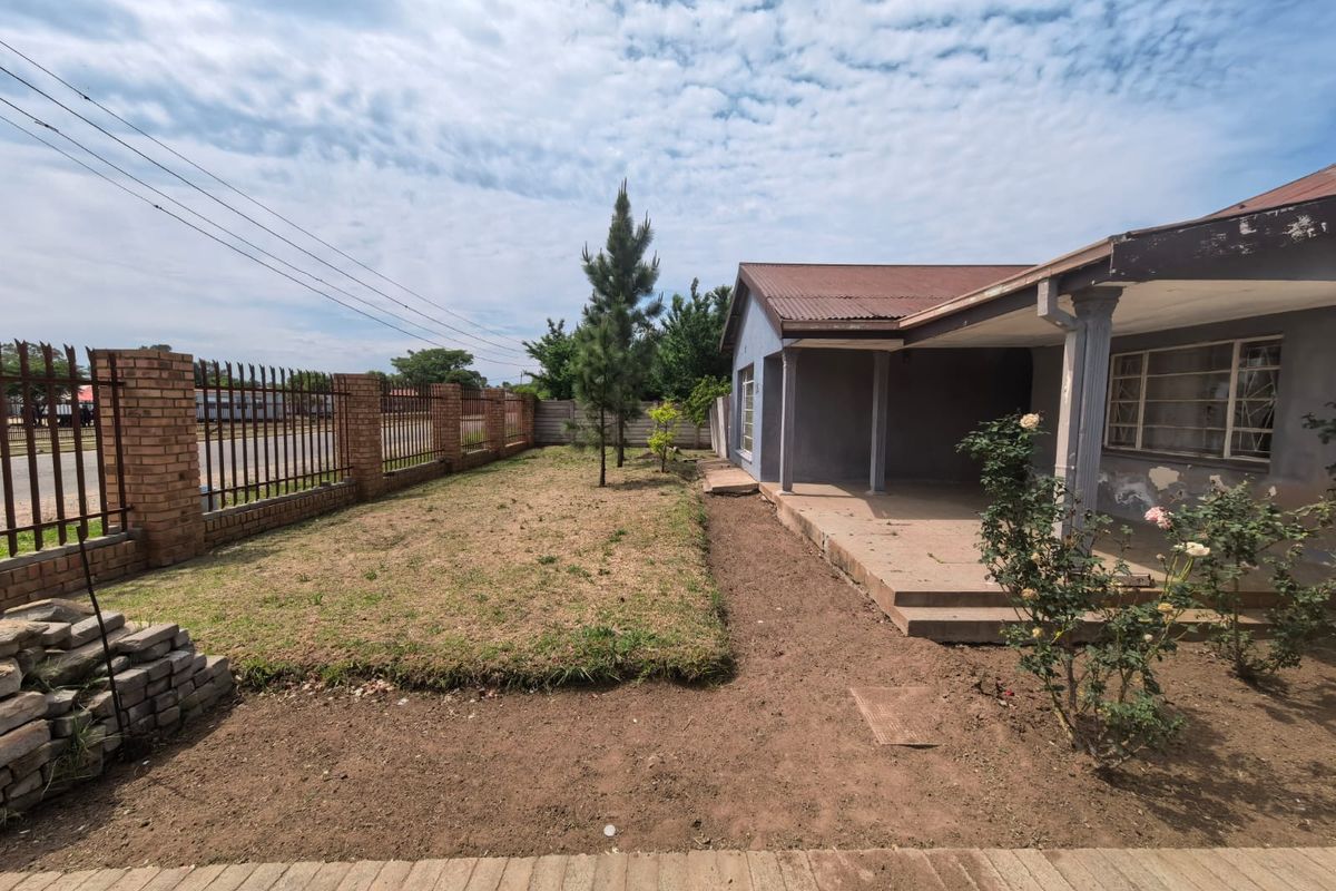 Front exterior view of a house featuring a covered patio, brick boundary wall with metal fencing, and a garden area requiring landscaping.