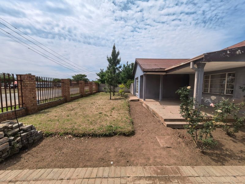 Front exterior view of a house featuring a covered patio, brick boundary wall with metal fencing, and a garden area requiring landscaping.