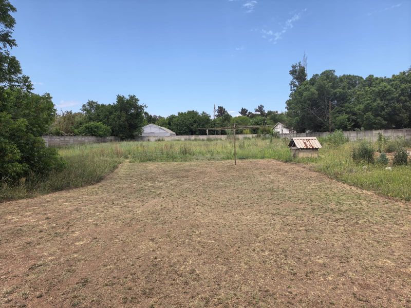 A large, open backyard featuring a precast concrete boundary wall, a rotary clothesline, and a rustic brick well structure set within a grassy area.