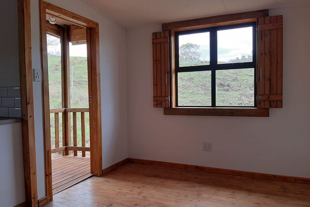 A bright, empty living area featuring warm timber flooring, rustic wooden window shutters, and direct access to an outdoor patio space.
