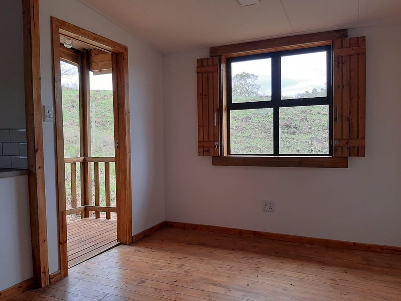 A bright, empty living area featuring warm timber flooring, rustic wooden window shutters, and direct access to an outdoor patio space.