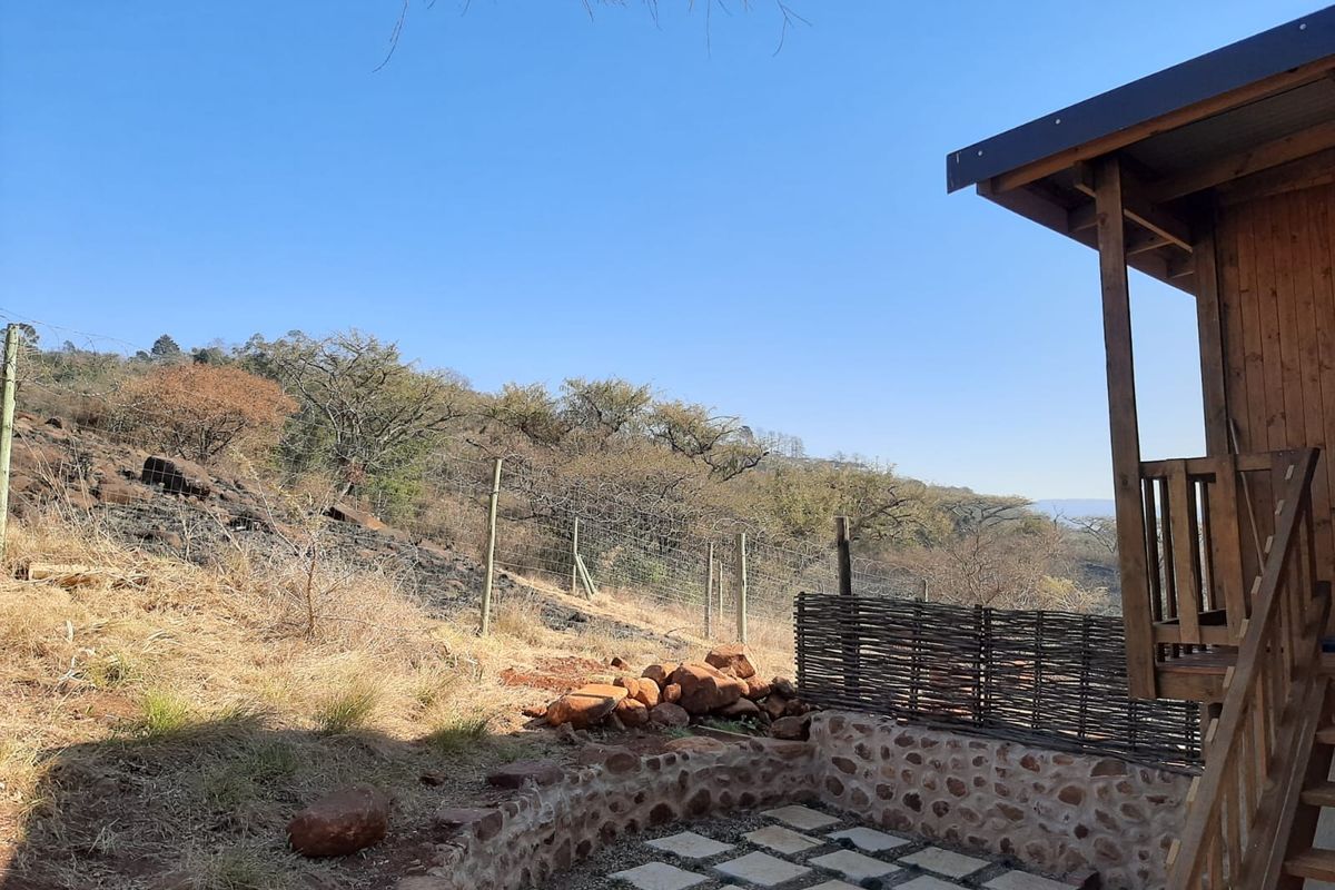 Rear exterior view of the cottage featuring a timber deck, stone retaining wall, and paved patio area overlooking the natural landscape.