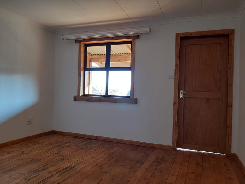 A clean, empty bedroom featuring warm timber flooring, a matching timber door, and a window with a timber frame.