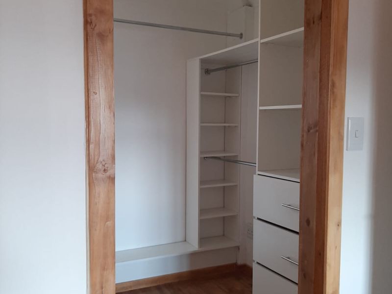 A clean, empty walk-in closet or dressing area featuring built-in white shelving, hanging rails, and warm-toned laminate flooring.
