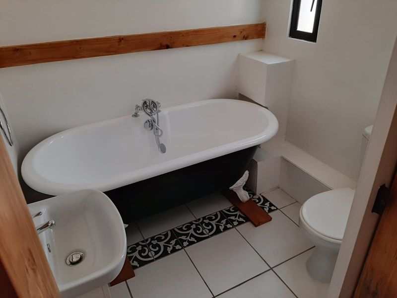 A clean, well-maintained bathroom featuring a classic freestanding bathtub, wall-mounted basin, toilet, and decorative tiled flooring with wooden accents.