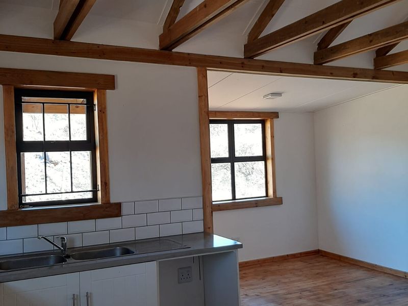 Open-plan living area featuring exposed timber roof trusses, timber flooring, and a functional kitchen corner with subway tile backsplash and built-in cabinetry.