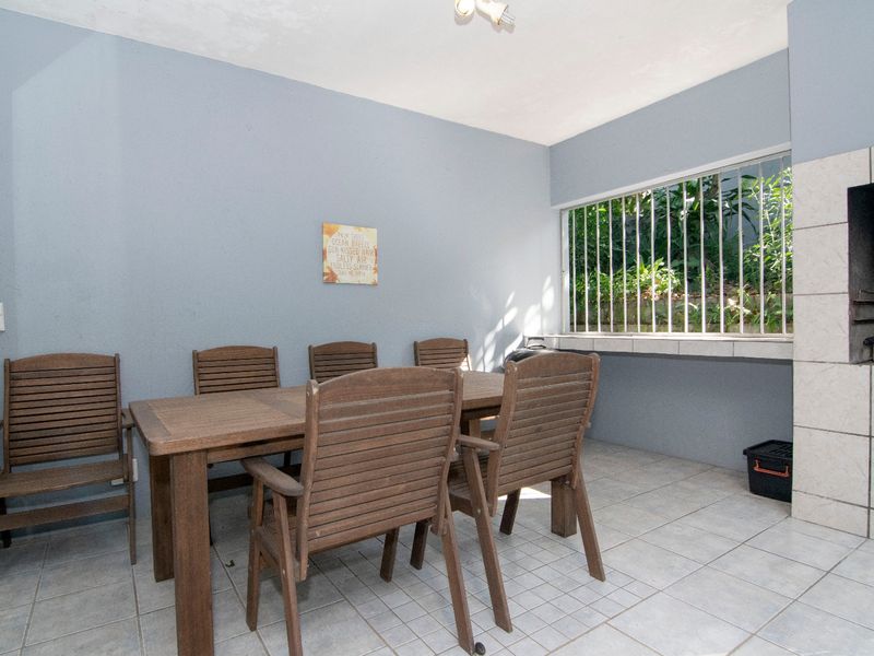 Covered patio area featuring a built-in braai, tiled flooring, and security bars on the window, providing a functional outdoor entertainment space.