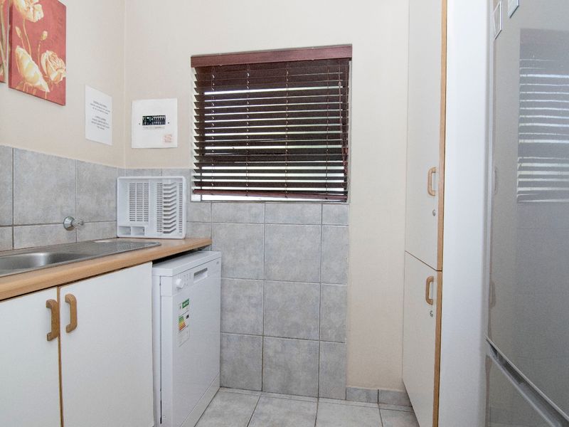 A functional laundry area featuring built-in cabinetry, a stainless steel sink, tiled splashbacks, and tiled flooring with a window for natural light.
