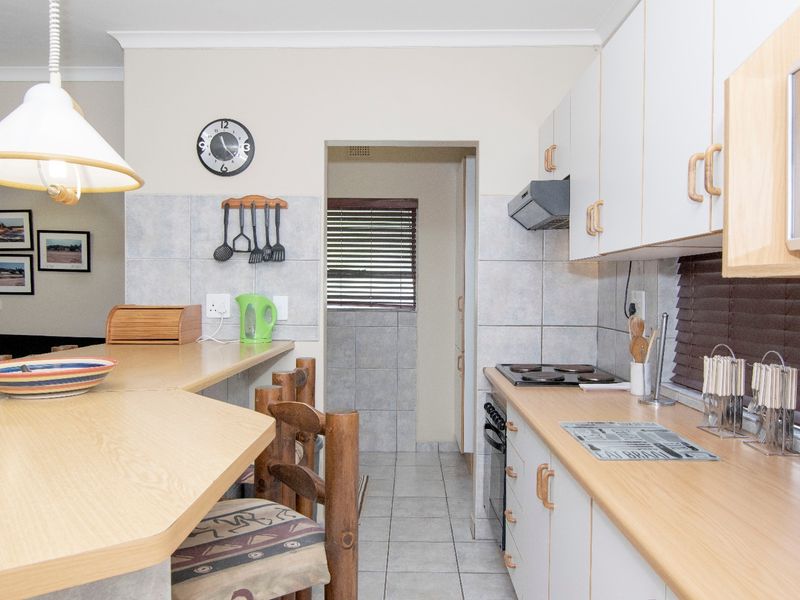 A functional kitchen featuring laminate countertops, built-in cabinetry, an electric hob, and a breakfast bar, with a tiled backsplash and flooring.
