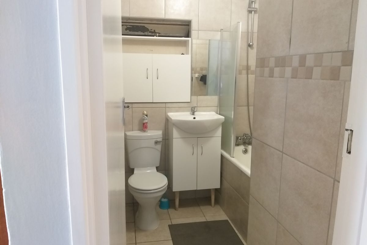 A functional bathroom featuring a bathtub with shower attachment, vanity basin, toilet, and neutral wall and floor tiling.