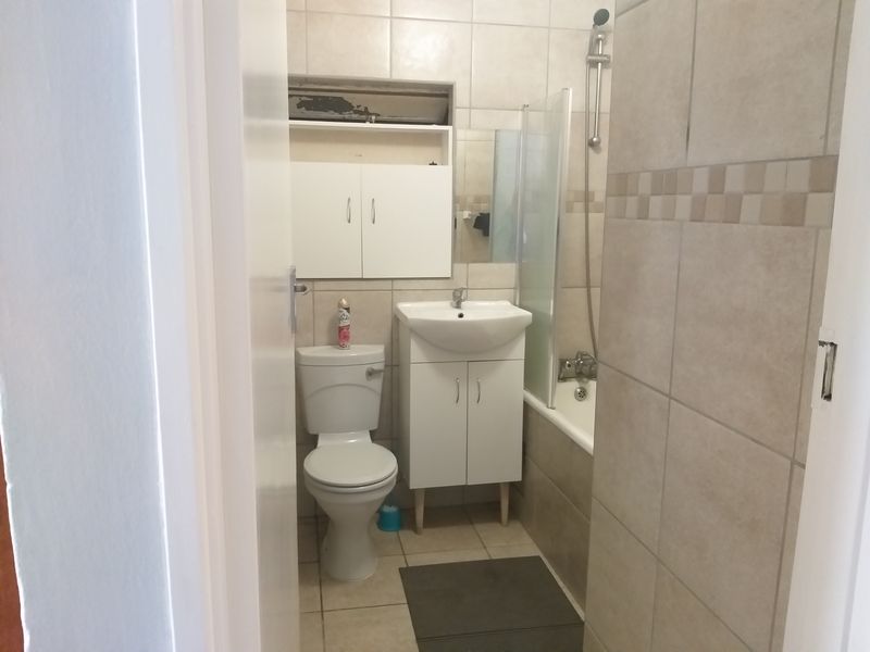 A functional bathroom featuring a bathtub with shower attachment, vanity basin, toilet, and neutral wall and floor tiling.