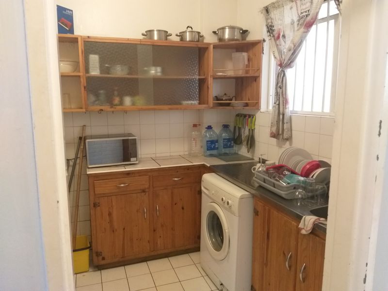 A compact scullery area featuring wooden cabinetry, tiled backsplash, and a stainless steel sink, providing functional utility space for the apartment.