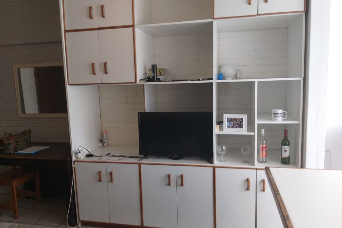 Living area featuring a large, white built-in wall unit with ample storage cabinetry and shelving against a textured brick wall.
