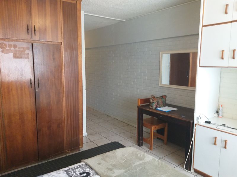 Bedroom featuring built-in wooden wardrobes, white storage cabinetry, tiled flooring, and a painted brick wall.