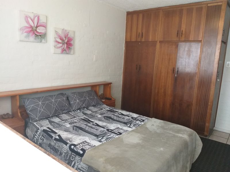 A bedroom featuring built-in wooden cupboards and a matching integrated headboard, offering functional storage space in a dated interior setting.