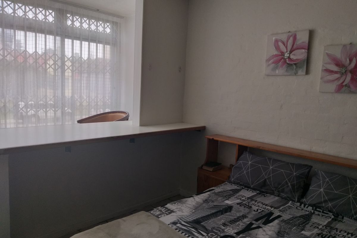 A bedroom featuring tiled flooring, a built-in desk area, and a window fitted with a security gate.