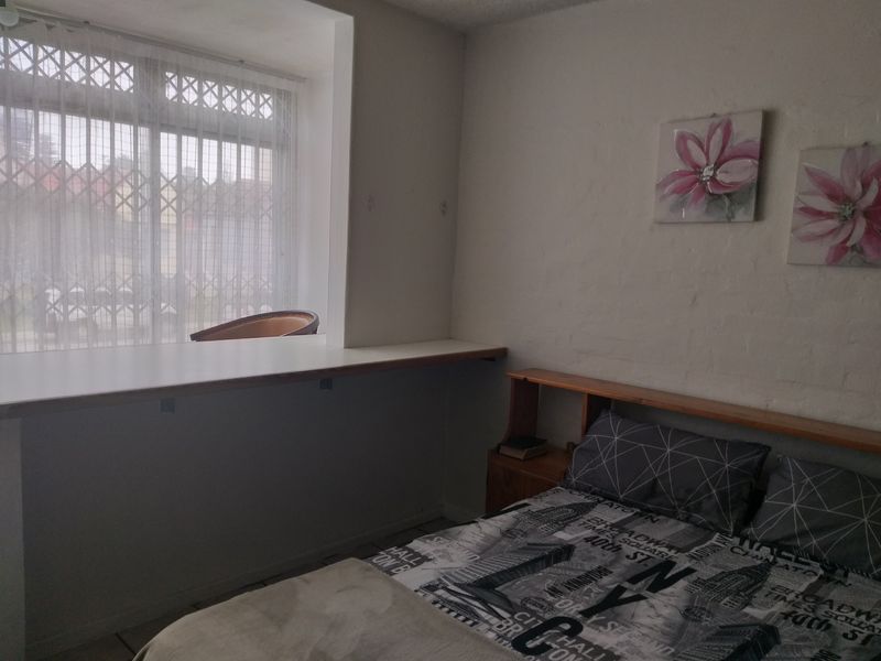 A bedroom featuring tiled flooring, a built-in desk area, and a window fitted with a security gate.