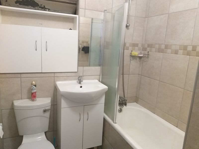 A functional bathroom featuring a vanity unit, toilet, and a bathtub with a glass shower screen, finished with neutral wall tiling.