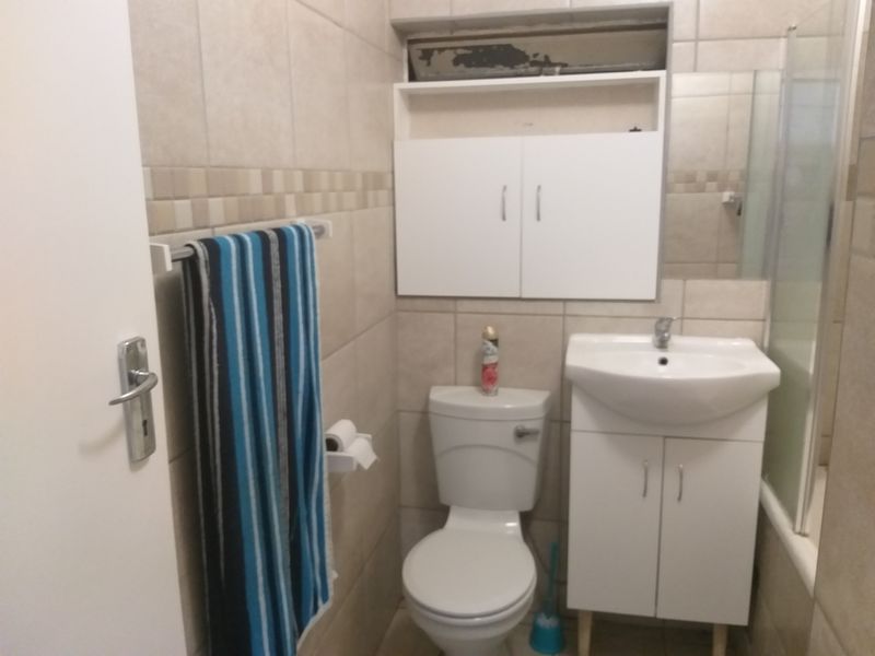 A functional bathroom featuring ceramic wall tiling, a vanity basin, a toilet, and a shower enclosure with a built-in storage cabinet.