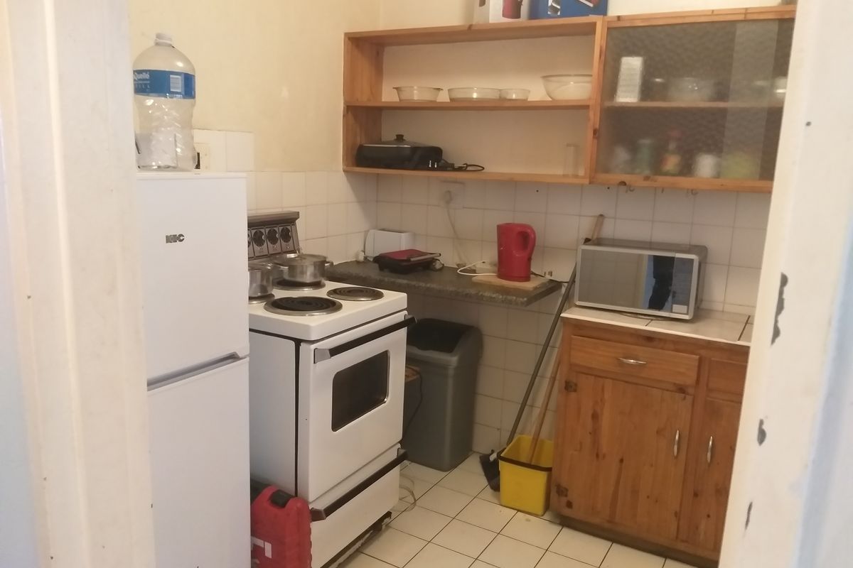 A compact kitchen featuring tiled flooring, a freestanding stove, wooden cabinetry, and open shelving, offering a functional layout with potential for modernization.