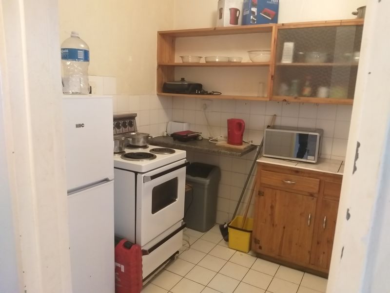 A compact kitchen featuring tiled flooring, a freestanding stove, wooden cabinetry, and open shelving, offering a functional layout with potential for modernization.