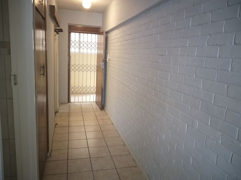 A functional apartment hallway featuring tiled flooring, a painted brick feature wall, and built-in storage cupboards, leading to a secure entrance.
