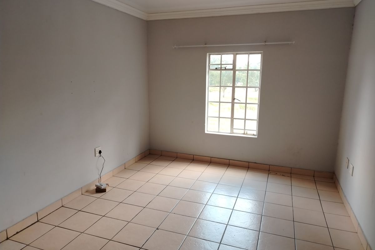 An empty bedroom featuring tiled flooring, neutral walls, and a window with security bars, providing a blank canvas for personalization.