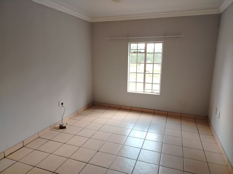 An empty bedroom featuring tiled flooring, neutral walls, and a window with security bars, providing a blank canvas for personalization.