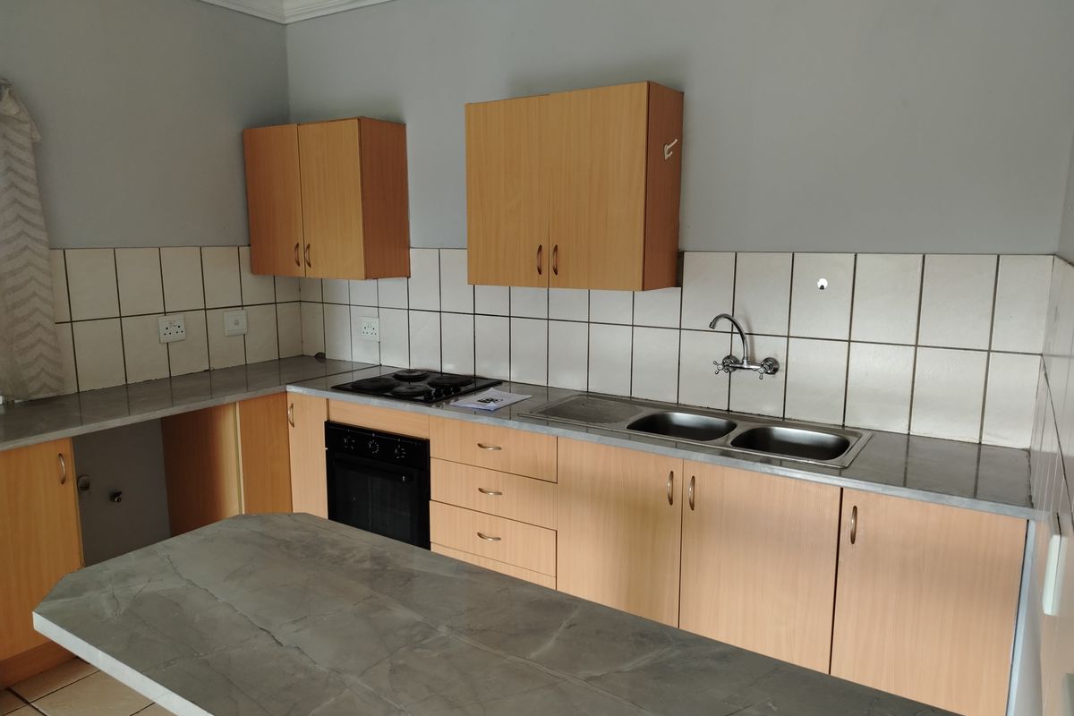 A functional kitchen featuring light wood-finish cabinetry, a double bowl sink, built-in oven, electric hob, and a central island with a stone-look countertop.