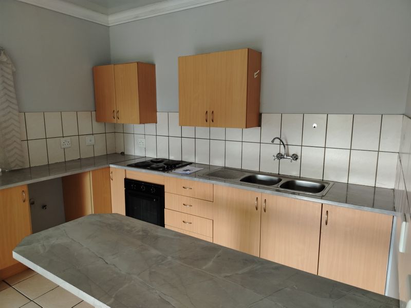 A functional kitchen featuring light wood-finish cabinetry, a double bowl sink, built-in oven, electric hob, and a central island with a stone-look countertop.