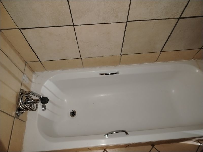 A standard bathroom bathtub featuring ceramic wall tiling and chrome fixtures, requiring minor maintenance to grout and sealant.