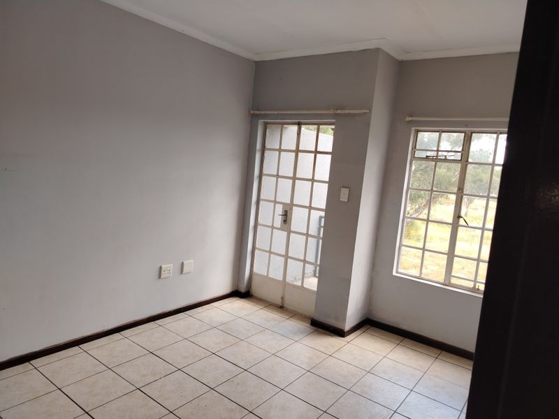 An empty living area featuring tiled flooring, a security gate, and windows with burglar bars, offering a neutral canvas for potential interior design.