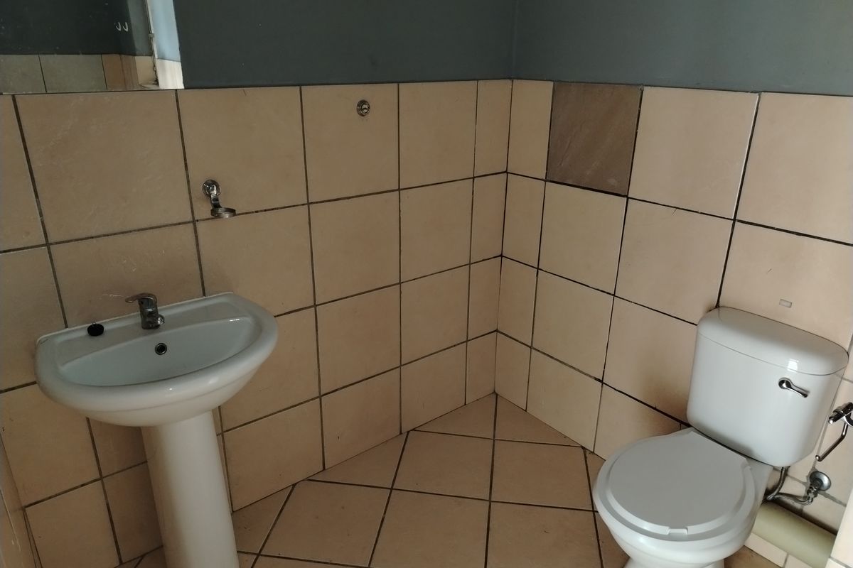 A compact bathroom featuring a pedestal basin, toilet, and tiled finishes. The space is vacant and ready for potential cosmetic updates.