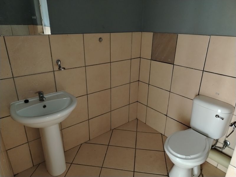 A compact bathroom featuring a pedestal basin, toilet, and tiled finishes. The space is vacant and ready for potential cosmetic updates.