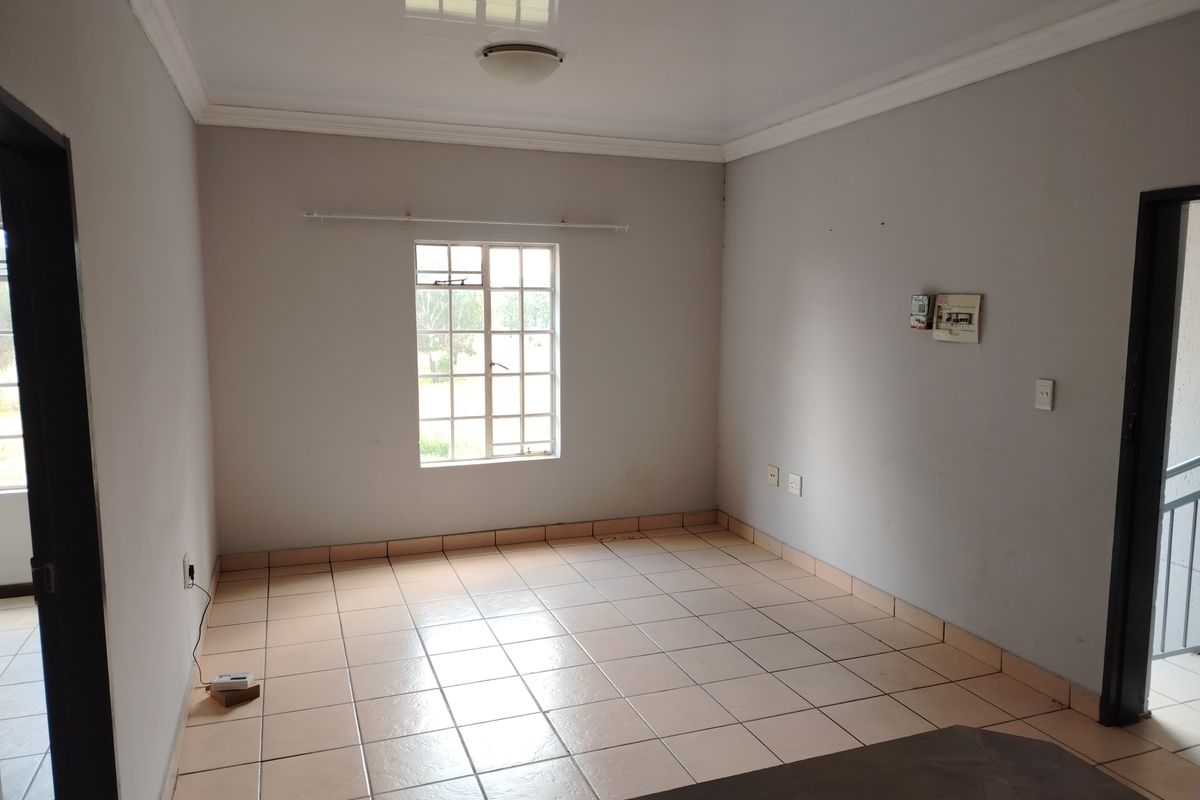 A vacant living area featuring neutral tiled flooring, ceiling cornice, and a window fitted with security burglar bars.